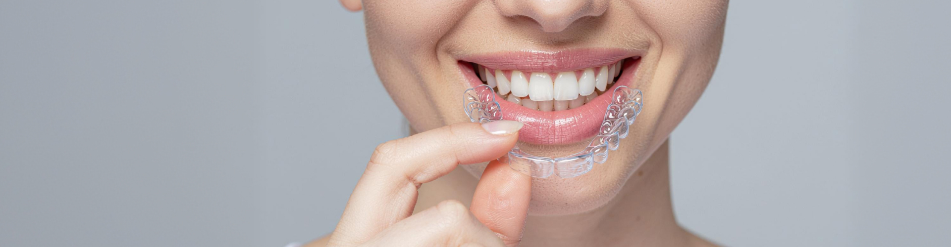 Woman holding clear aligner in front of smile.